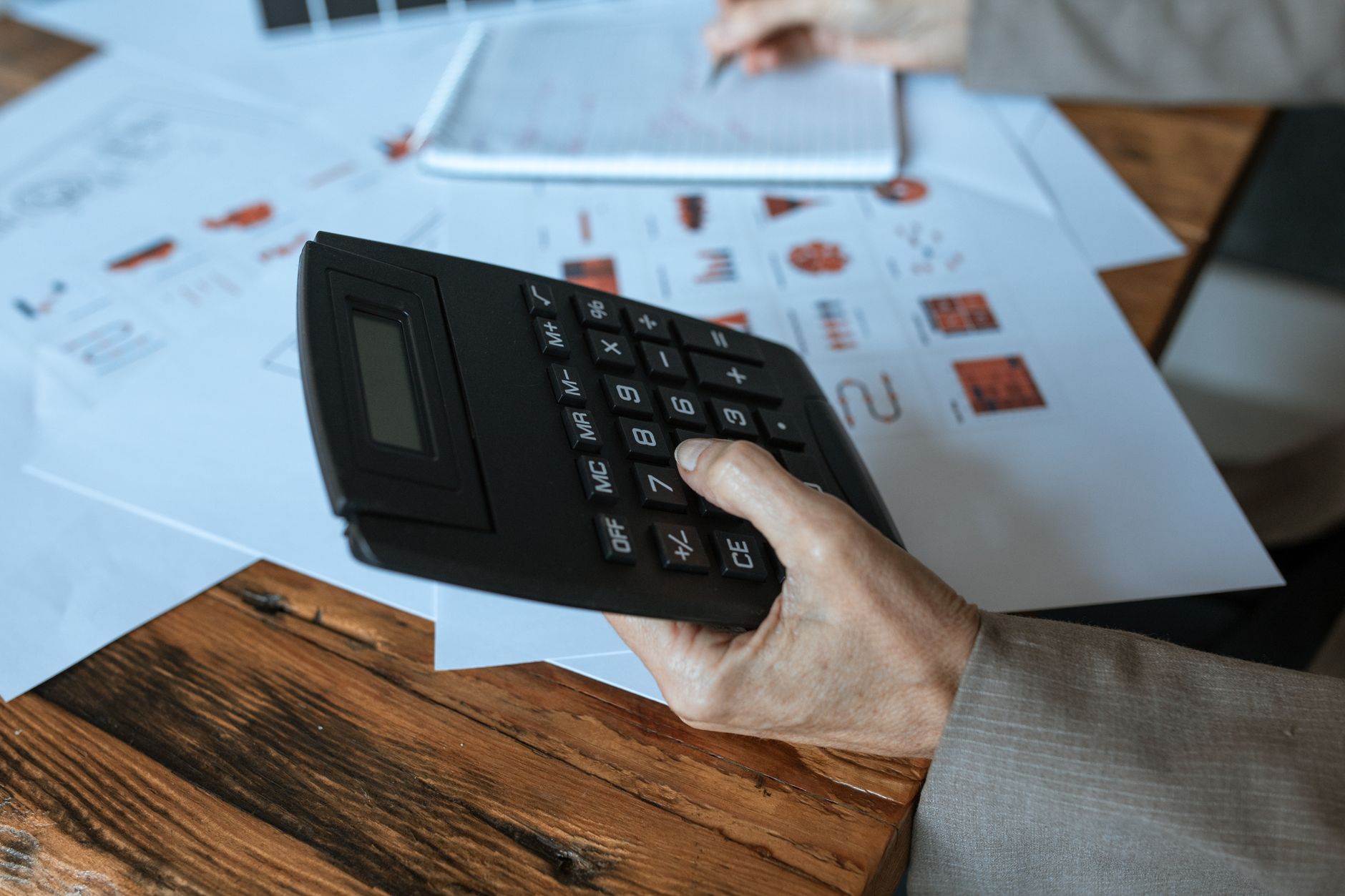 main posée sur une calculatrice au-dessus de feuilles de calcul et de graphiques imprimés, sur un bureau en bois