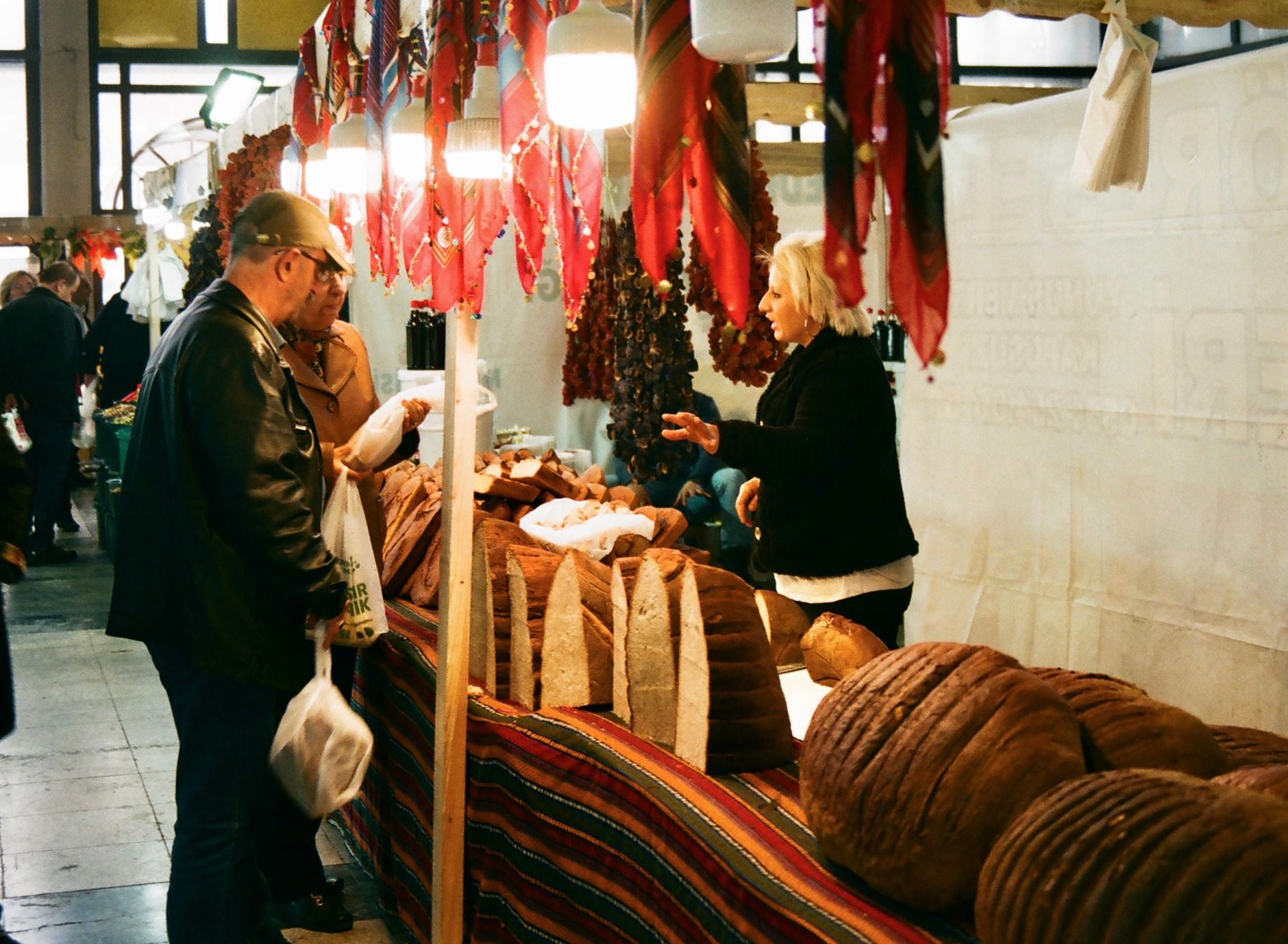 marchande de pain qui échange avec des clients devant son étal sur un marché couvert