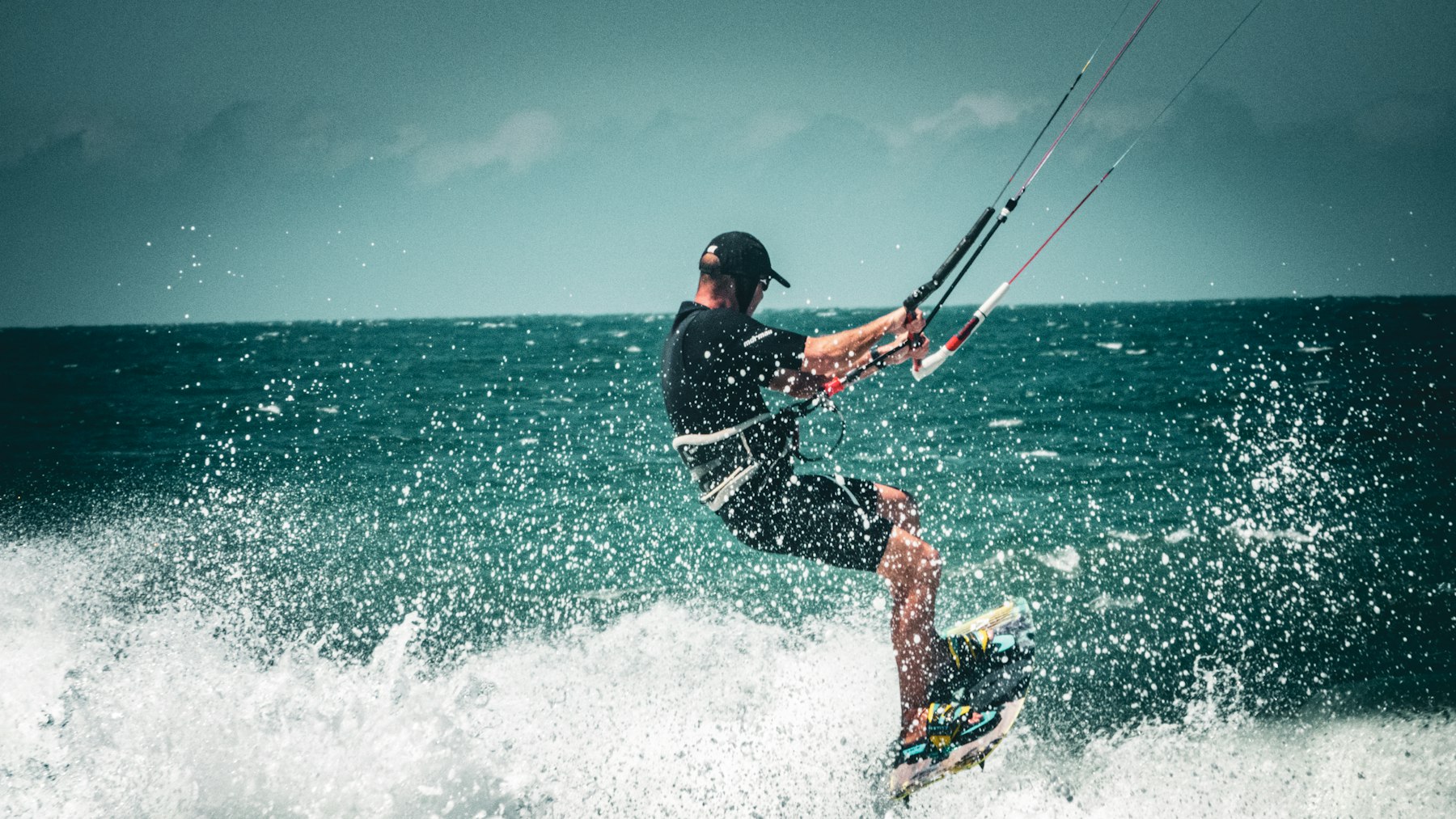 kitesurfeur de dos qui tire sur la barre de son aile dans une mer formée, éclaboussures autour de la planche