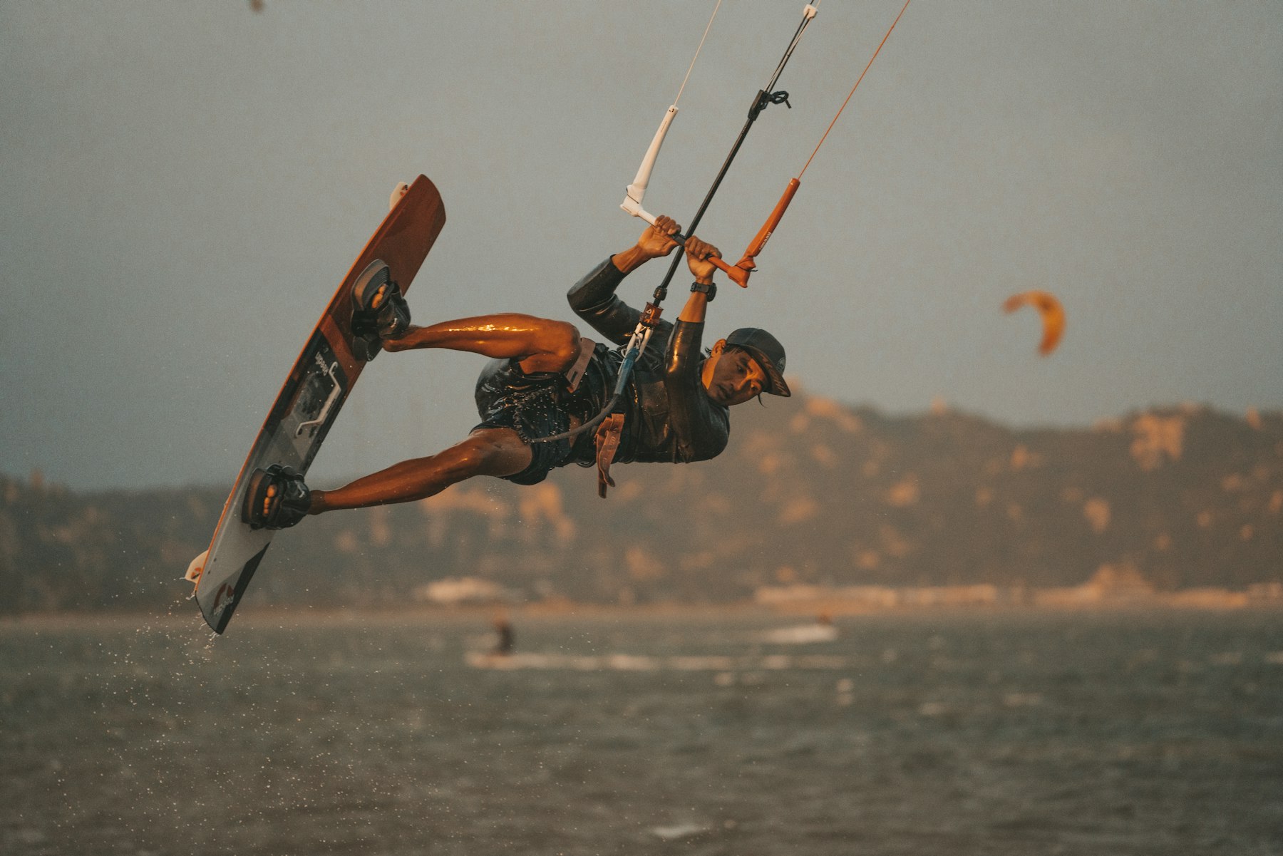 kitesurfeur en plein saut au-dessus de l'eau, planche tenue en main, aile visible en arrière-plan