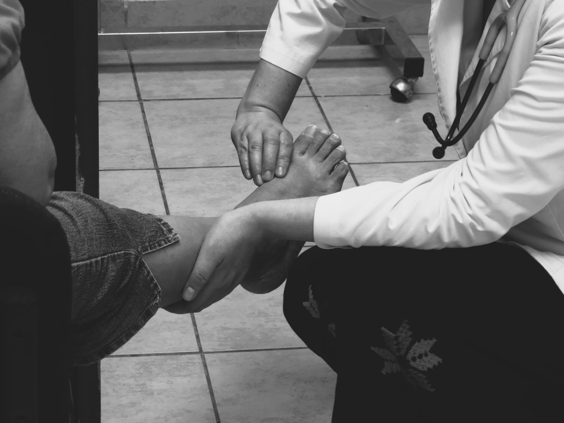 professionnel de santé en blouse blanche tenant et examinant le pied d'un patient assis